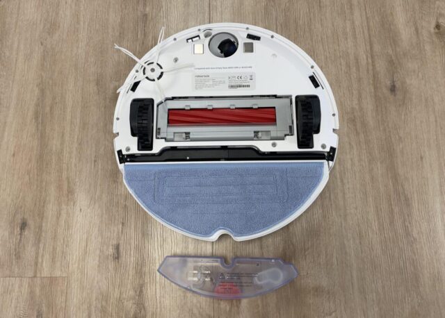 Der Roborock S7 Staubsauger Roboter Ansicht der Unterseite, zu sehen: Hauptbürste, Seitenbürste, Wischmodul mit Aufsatz, Räder und Sensoren